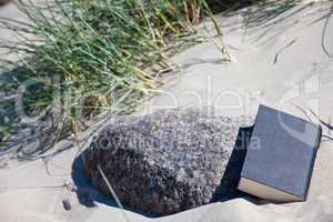 Schwarzes Buch lehnt am Stein in einer Düne