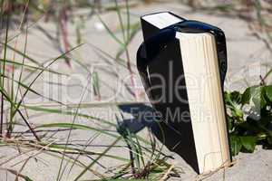 Sonnenbrille hängt über einem Buch am Strand