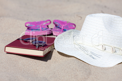 Nahaufnahme Strohhut und Buch am Strand