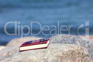 Buch mit Sonnenbrille auf Felsen am Strand