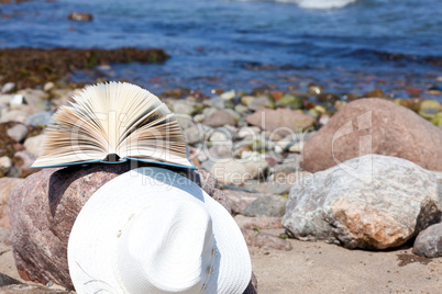 Strohhut und Buch liegen an einem Felsen der Ostseeküste
