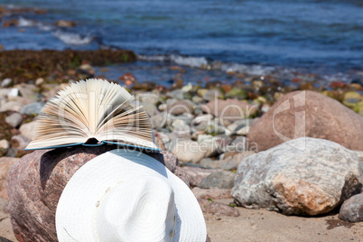 Strohhut und Buch liegen an einem Felsen der Ostseeküste