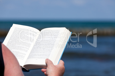 Hände halten Buch im Hintergrund das Meer