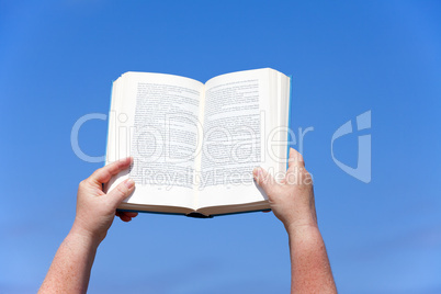 Hände halten ein Buch gegen den blauen Himmel