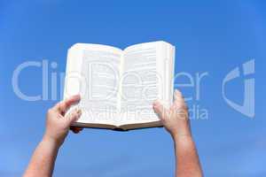 Hände halten ein Buch gegen den blauen Himmel