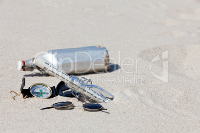 Kompass, Feldflasche und Flaschenpost in der Wüste