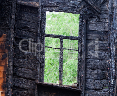Burned wooden window frame with view to a green trees
