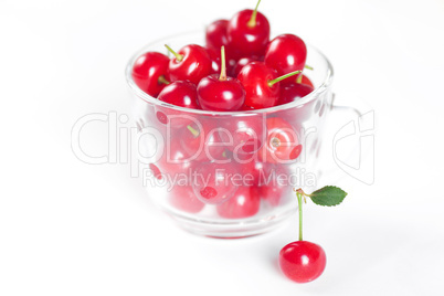 cherry with green leaf and a cup of cherries on a white background