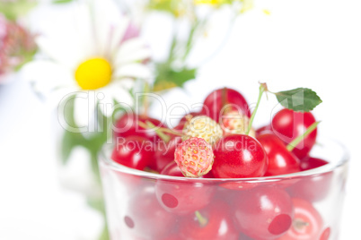 glass cup with cherries and wild strawberries and a bouquet of w