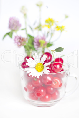 glass cup with cherries and a bouquet of wildflowers