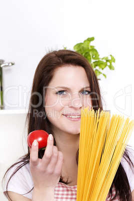 lächelnde junge frau hält tomate und spaghetti
