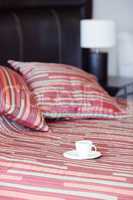 bed with a pillow, a cup of tea on the bedside table and lamp