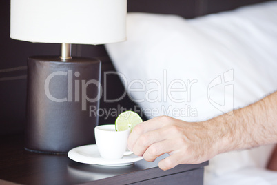 man hand, a cup of tea on the bedside table and lamp
