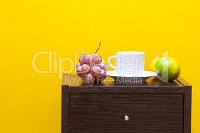 bedside table,fruits and cup against a yellow wall in the apartm