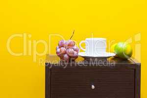 bedside table,fruits and cup against a yellow wall in the apartm