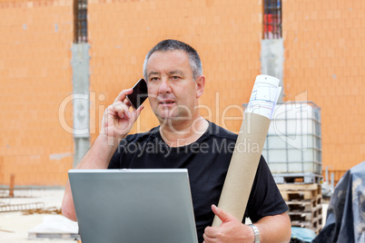 Civil engineer with blueprint and a laptop on site