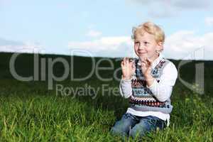 Impish little boy kneeling in green field