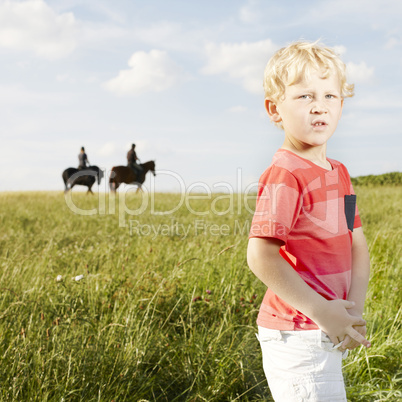 Young blonde boy standing in a grassy field