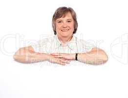 Aged woman standing behind blank billboard