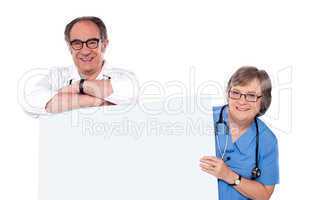 Two matured doctors holding white banner ad