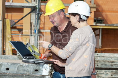 Civil engineer and construction worker looking at the laptop
