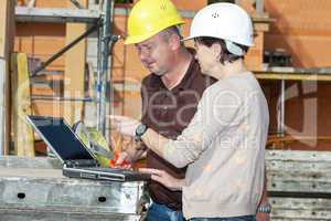 Civil engineer and construction worker looking at the laptop