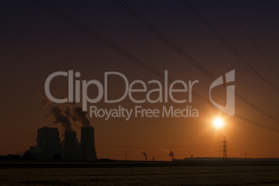 Brown coal power plant with cooling towers and steam and powerlines during sunset with red sky