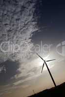Wind Turbine with clouds in the sky and the sun shining behind the turbine