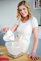 Smiling woman pouring water in flour bowl