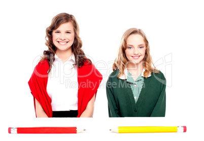 Big pencils lying in front of two school girls