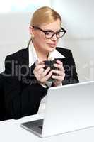 Female executive looking at laptop holding mug