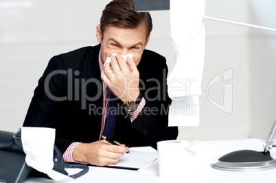Professional sitting at desk sneezing into tissue