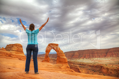 Woman with raised hands in front of Delicate Arch