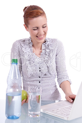 Junge Frau mit Laptop und Snack am Schreibtisch