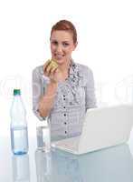 Junge Frau mit Laptop und Snack am Schreibtisch