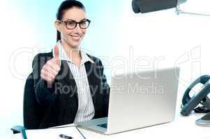 Young businesswoman sitting on desk  gesturing thumbs up