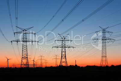 Strommasten bei Sonnenuntergang mit Windrädern am Horizont