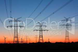 Strommasten bei Sonnenuntergang mit Windrädern am Horizont