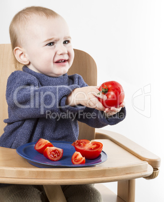 young child eating tomatoes in high chair