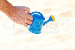 hand of a man with a watering can on a background of sand
