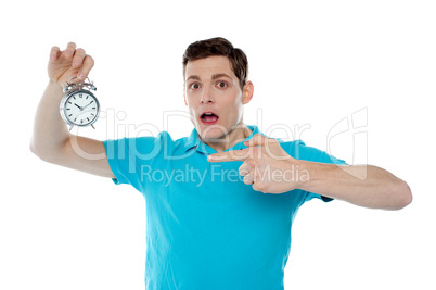 Shocked young guy holding alarm clock