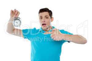 Shocked young guy holding alarm clock