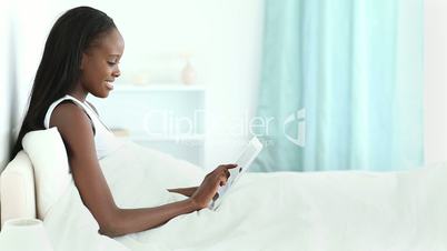 Woman lying in her bed while typing on a tablet tactile