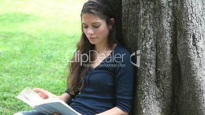 Woman sitting against a tree while reading a book