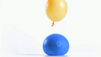 Yellow balloon rebounding in super slow motion on a blue one