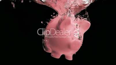 Pink piggy-bank falling in super slow motion into water