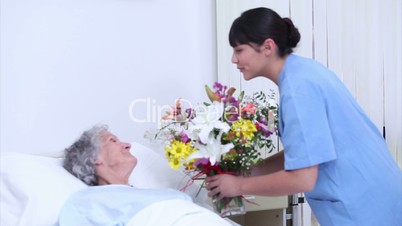 Serene senior woman speaking at a nurse who gives a bouquet of flowers