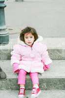 Little girl in winter clothes sitting in stairs looking at the c