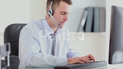 Businessman typing at computer while speaking with headset