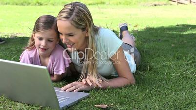 Mother and his daughter using a laptop in a park